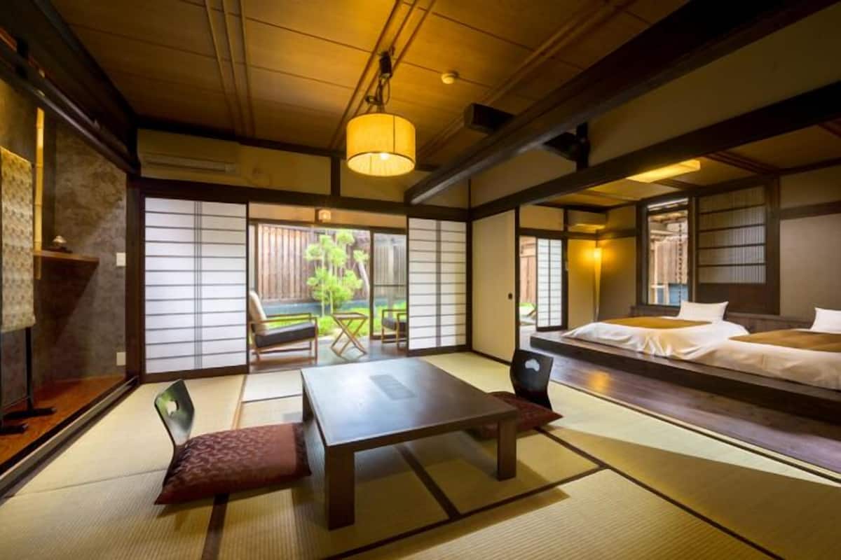 A traditional Japanese room with tatami flooring, a low table, and a bed with white bedding.