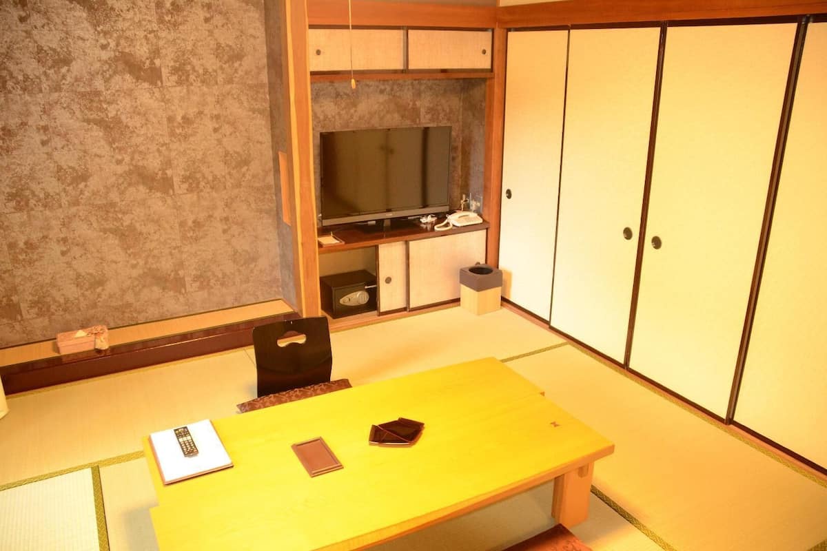 A room with tatami flooring, a low table, a television, and traditional sliding doors.