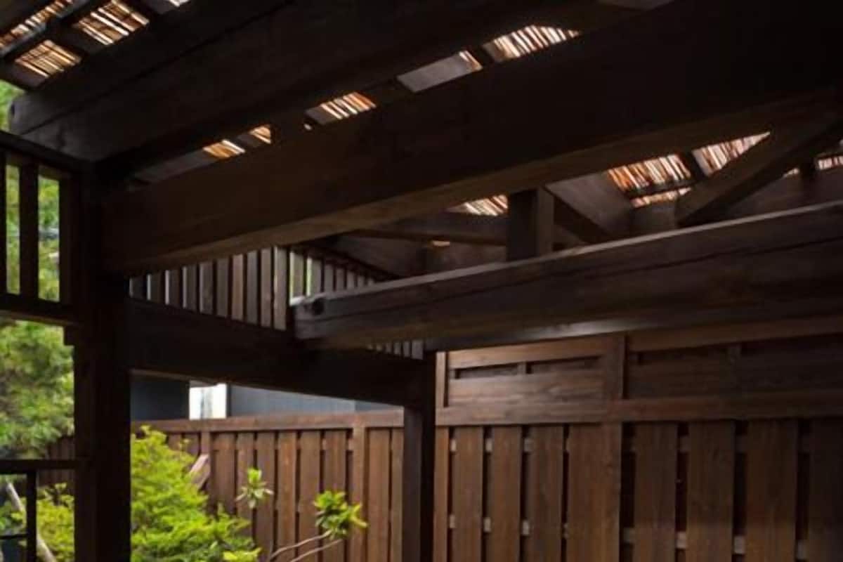 A hot tub under a wooden pergola with a wooden fence in the background.