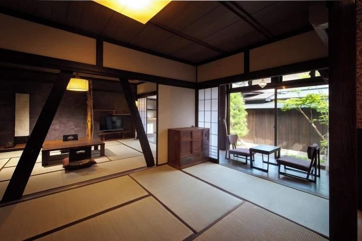 Une pièce de style japonais traditionnel, avec un sol recouvert de tatamis, une table basse, un meuble et des portes coulissantes donnant sur un espace extérieur.