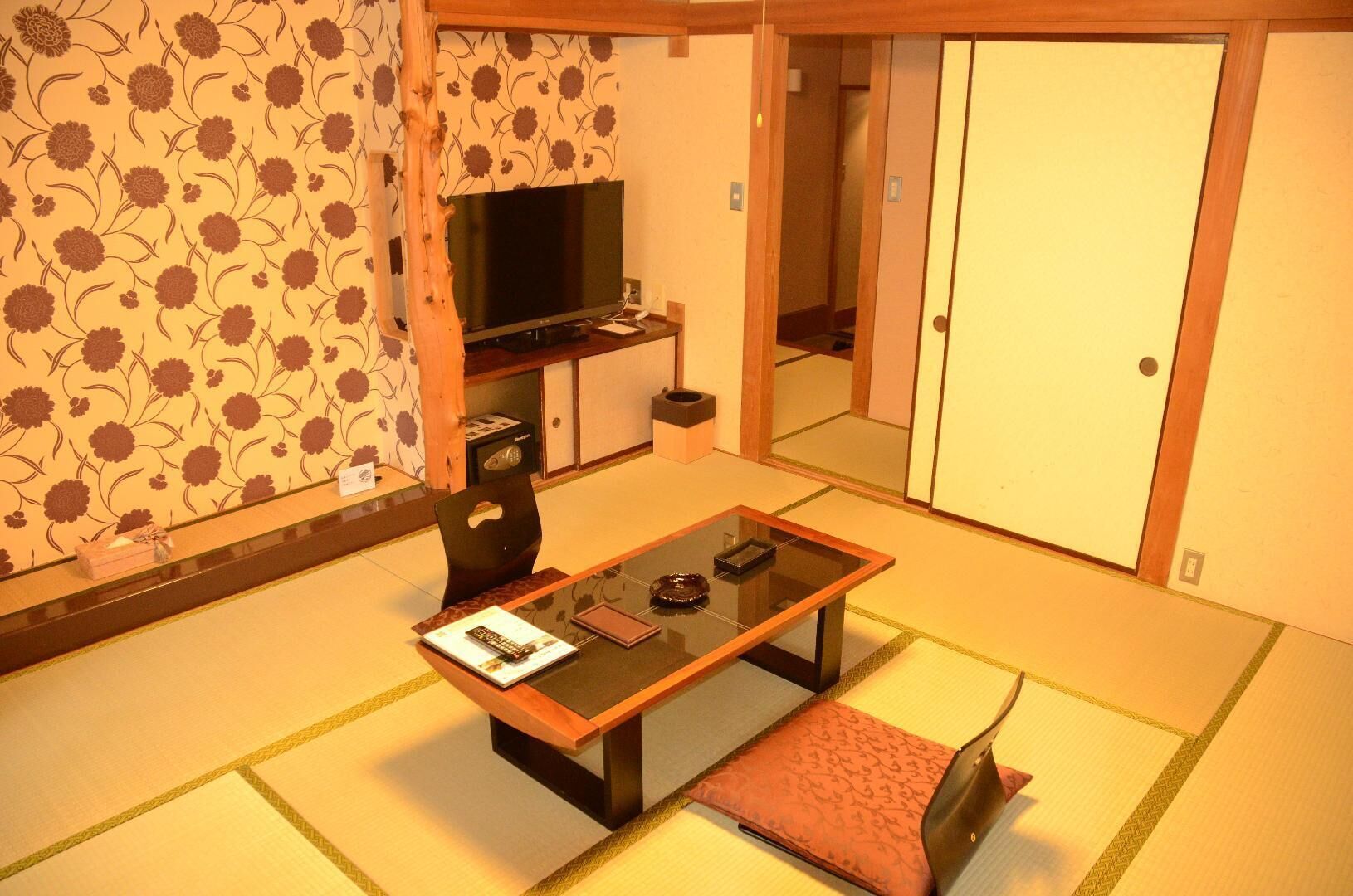 A traditional Japanese room with tatami flooring, a low table with cushions, a television, and sliding doors.