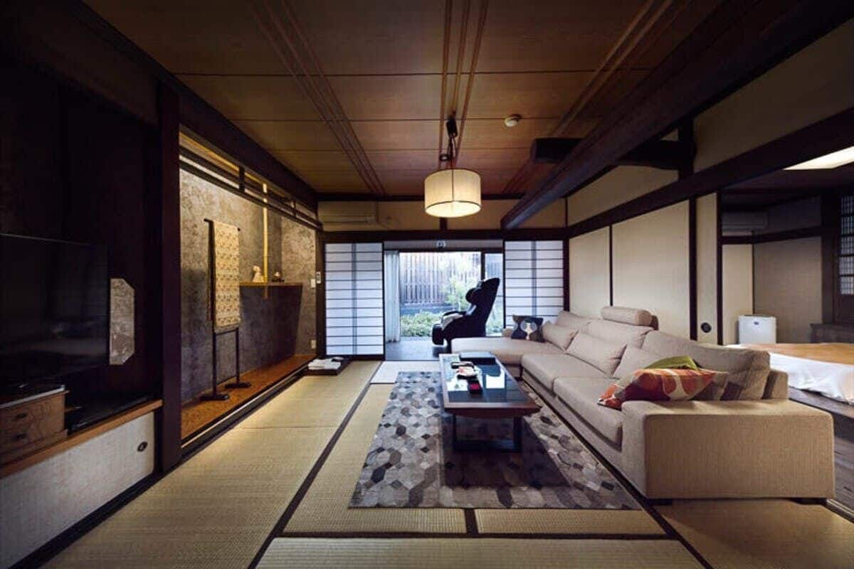 A traditional Japanese-style living room with tatami flooring, a low sofa, a coffee table, and sliding doors leading to a garden.