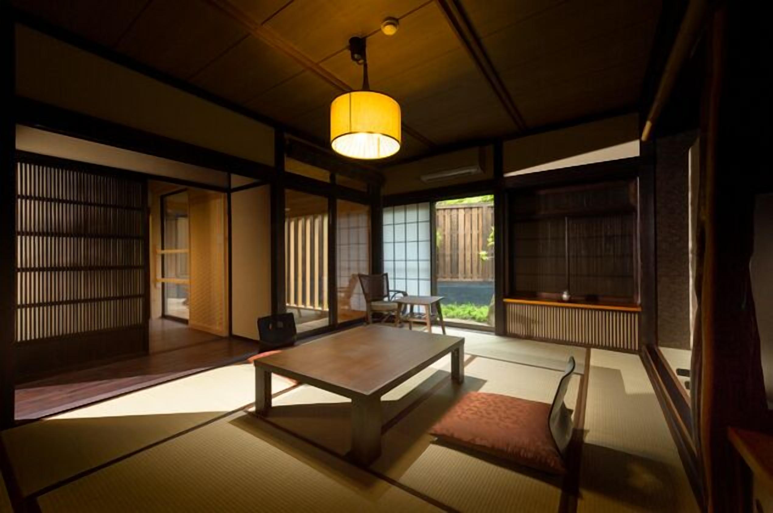 A traditional Japanese room with tatami flooring, a low table, a chair, and a hanging lamp.