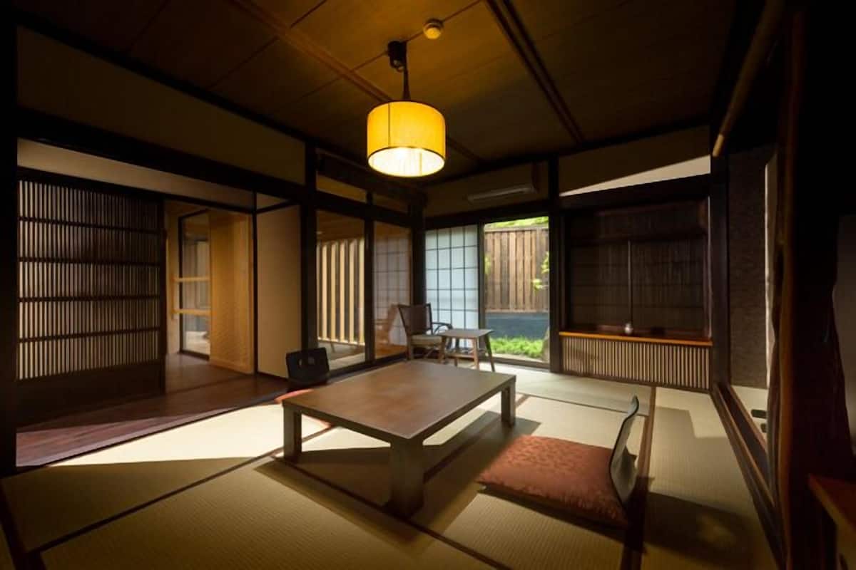 A traditional Japanese room with tatami flooring, a low table, a chair, and a hanging lamp.