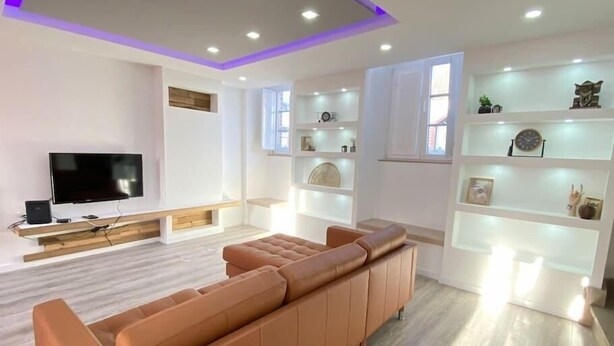 Een moderne woonkamer met een grote flatscreen-tv, een bruine leren bank en inbouwkasten met decoratieve objecten.