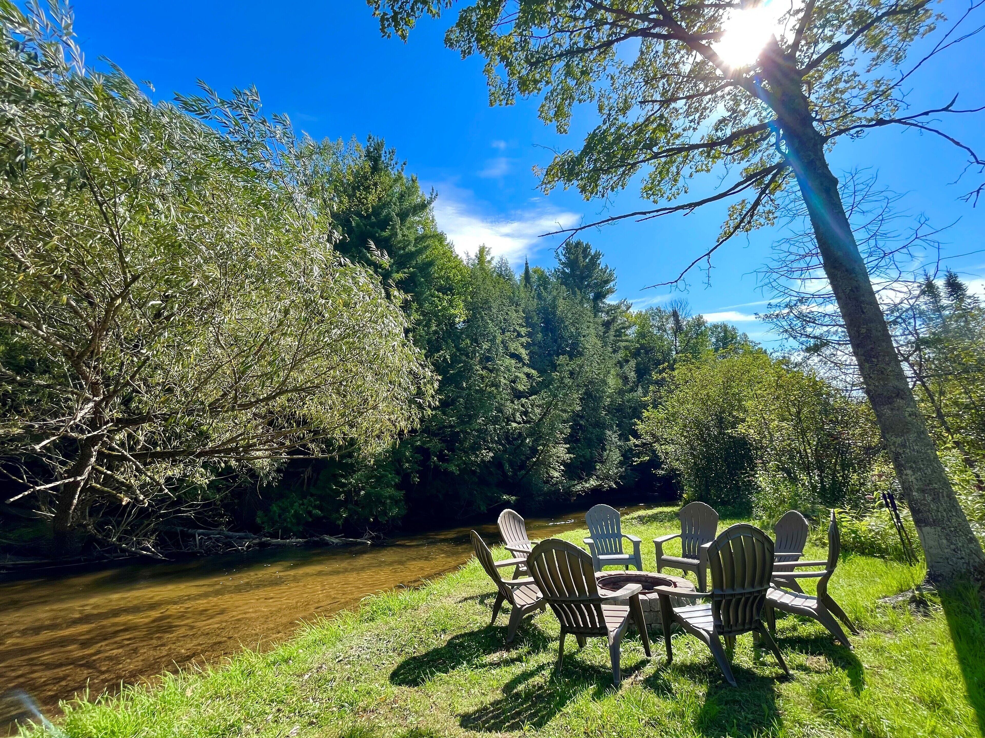 Eine Uferlandschaft mit Tisch und Stühlen, umgeben von Bäumen und Grün.
