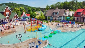 Un espace piscine comprenant une structure de jeux aquatiques, des chaises longues et un terrain de basket-ball.