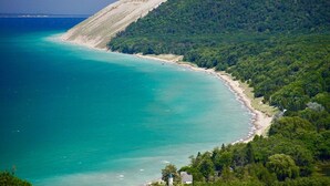 Un paysage côtier comprenant une plage, des collines boisées et une vue dégagée sur la mer.