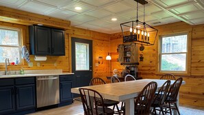 A cozy cabin-style kitchen with a central island, wooden cabinets, and a dining area with chairs. - Play & Stay near State Parks & Seven Springs (Champion)