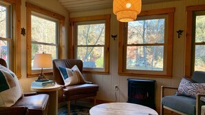 A cozy room with wooden walls, large windows, a fireplace, and a round wooden table. - Play & Stay near State Parks & Seven Springs (Champion)