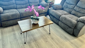 Un soggiorno con due divani grigi, un tavolino in legno con un'orchidea in vaso e un'ampia finestra con tende.