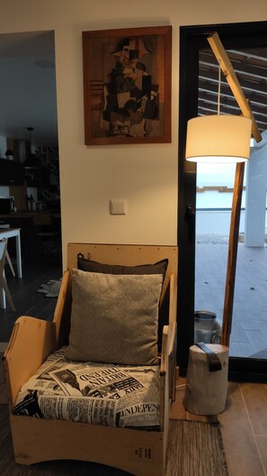 A room with a wooden bed, a newspaper-filled cardboard box, a lamp, and a painting on the wall. - Laranjeira das Loiras (Obidos)