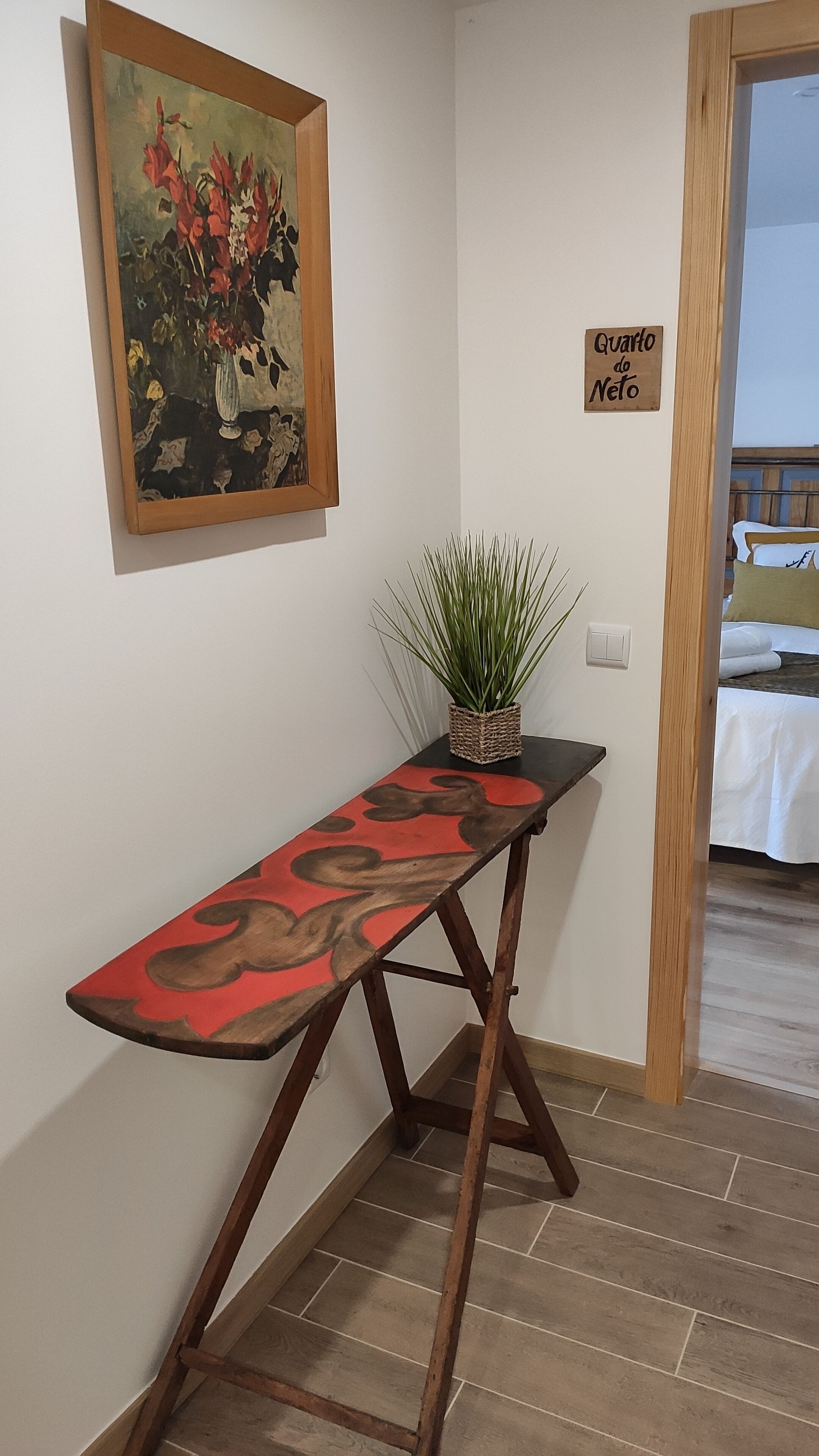 Een hal met een houten bankje, een potplant, een schilderij en een bordje met de tekst 