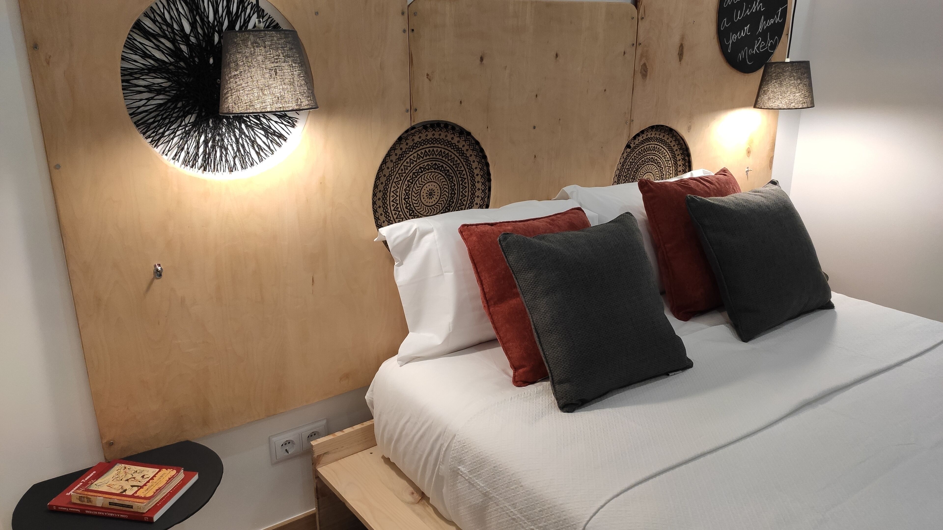 A neatly made bed with white and dark grey pillows, a wooden headboard, and two wall-mounted lamps.