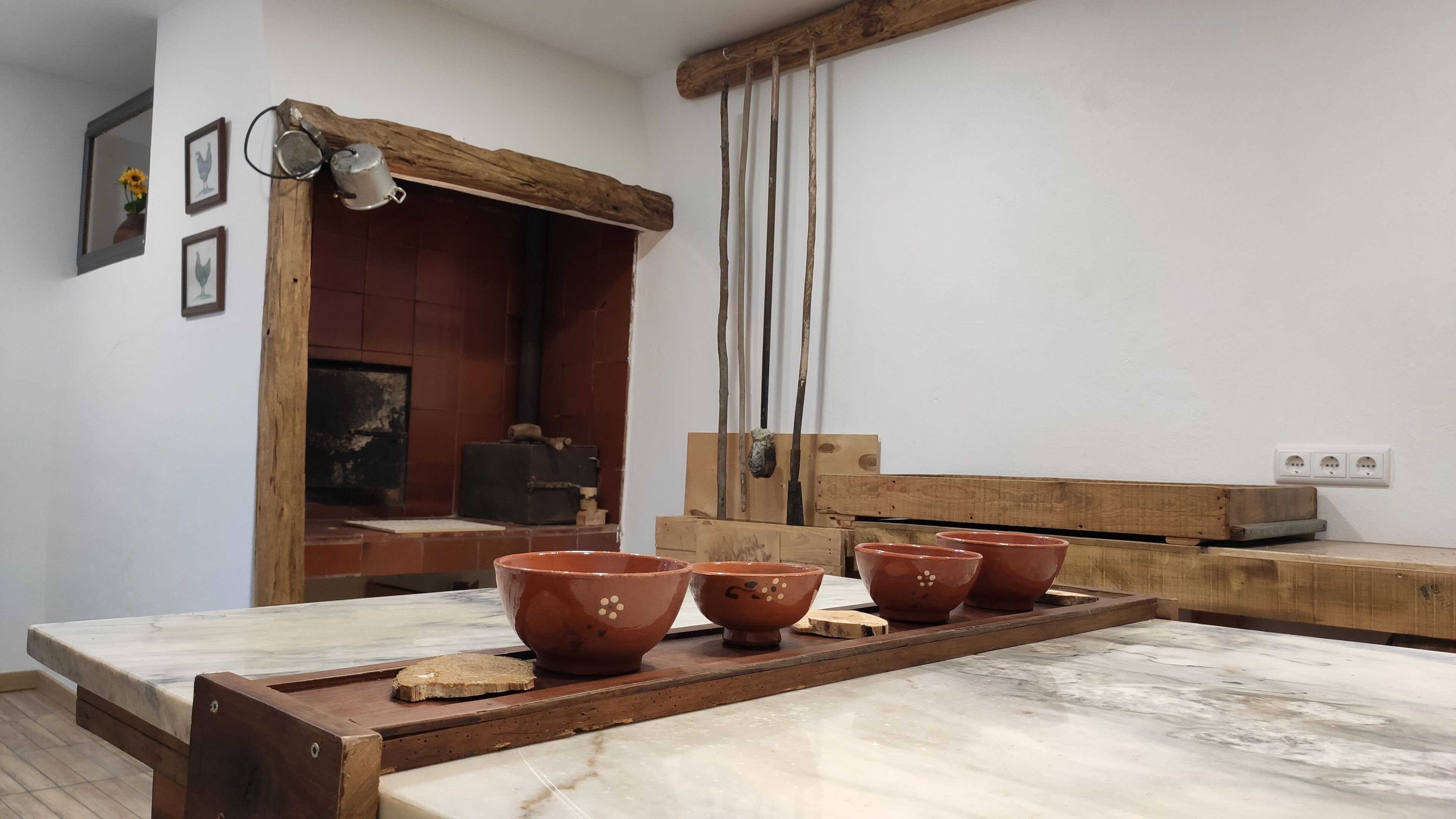 A rustic kitchen with a wooden table, terracotta pots, and a brick oven.