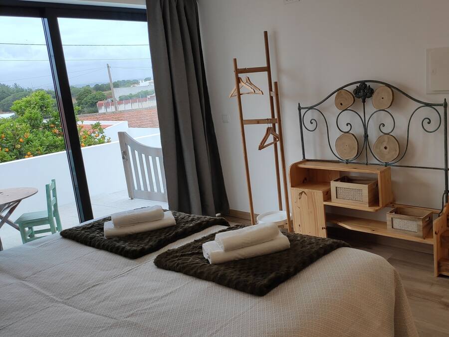A hotel room with a balcony, a bed with a headboard, a wooden side table, and a chair.