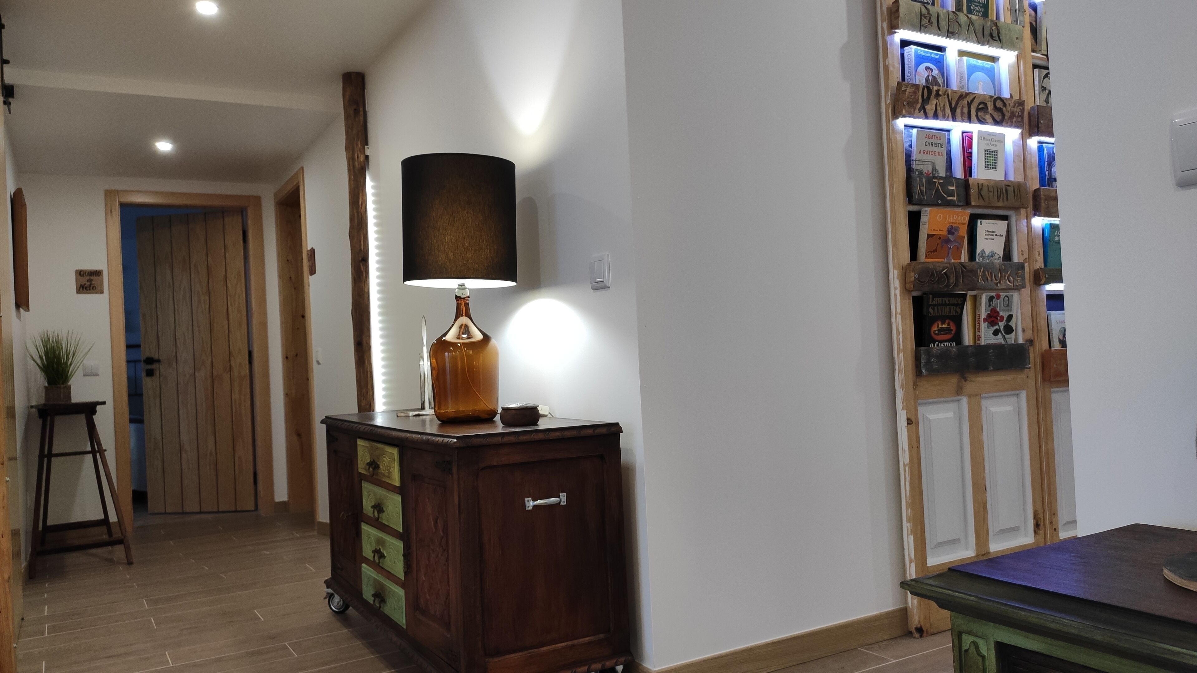 A hallway with a wooden cabinet, a lamp, and a wall with framed pictures.