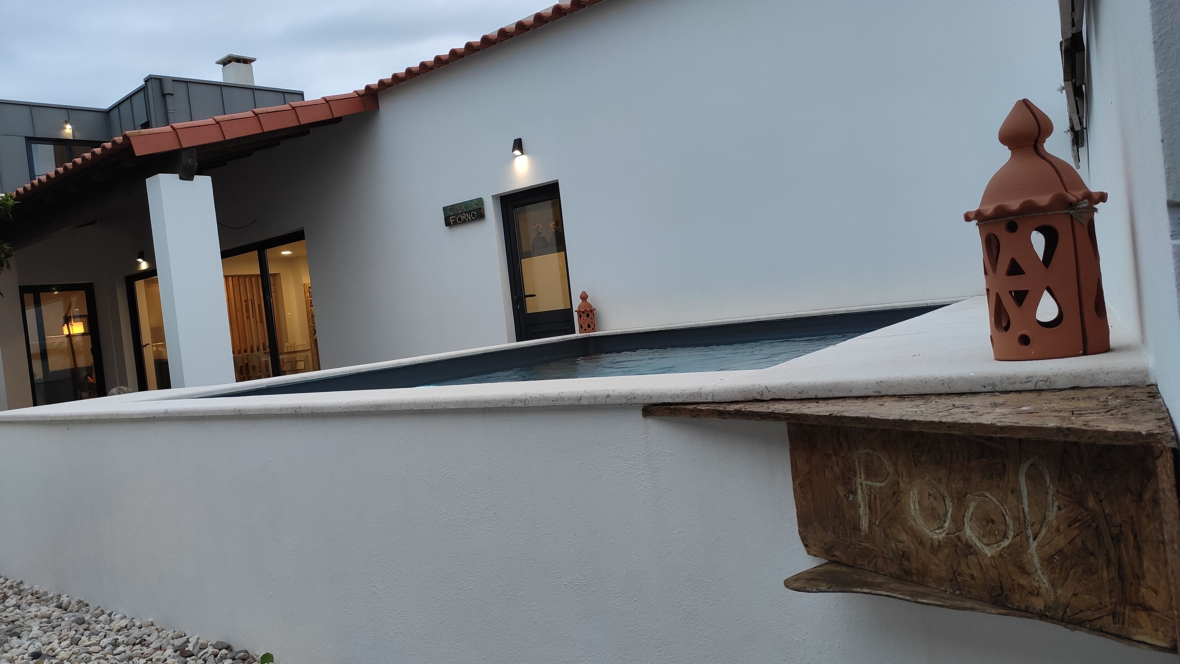 Um edifício moderno com fachada branca, uma piscina pequena e uma placa de madeira com a inscrição 'Fool'.