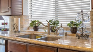 Una cocina con pileta doble, encimera de granito, muebles de madera y plantas en macetas.