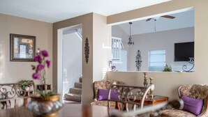 Un salón con una mesa de comedor de madera, sillas con estampado floral, una araña y un televisor montado en la pared.