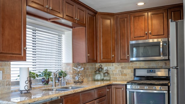 Una cocina con armarios de madera, electrodomésticos de acero inoxidable, encimera de granito y una ventana con persianas.