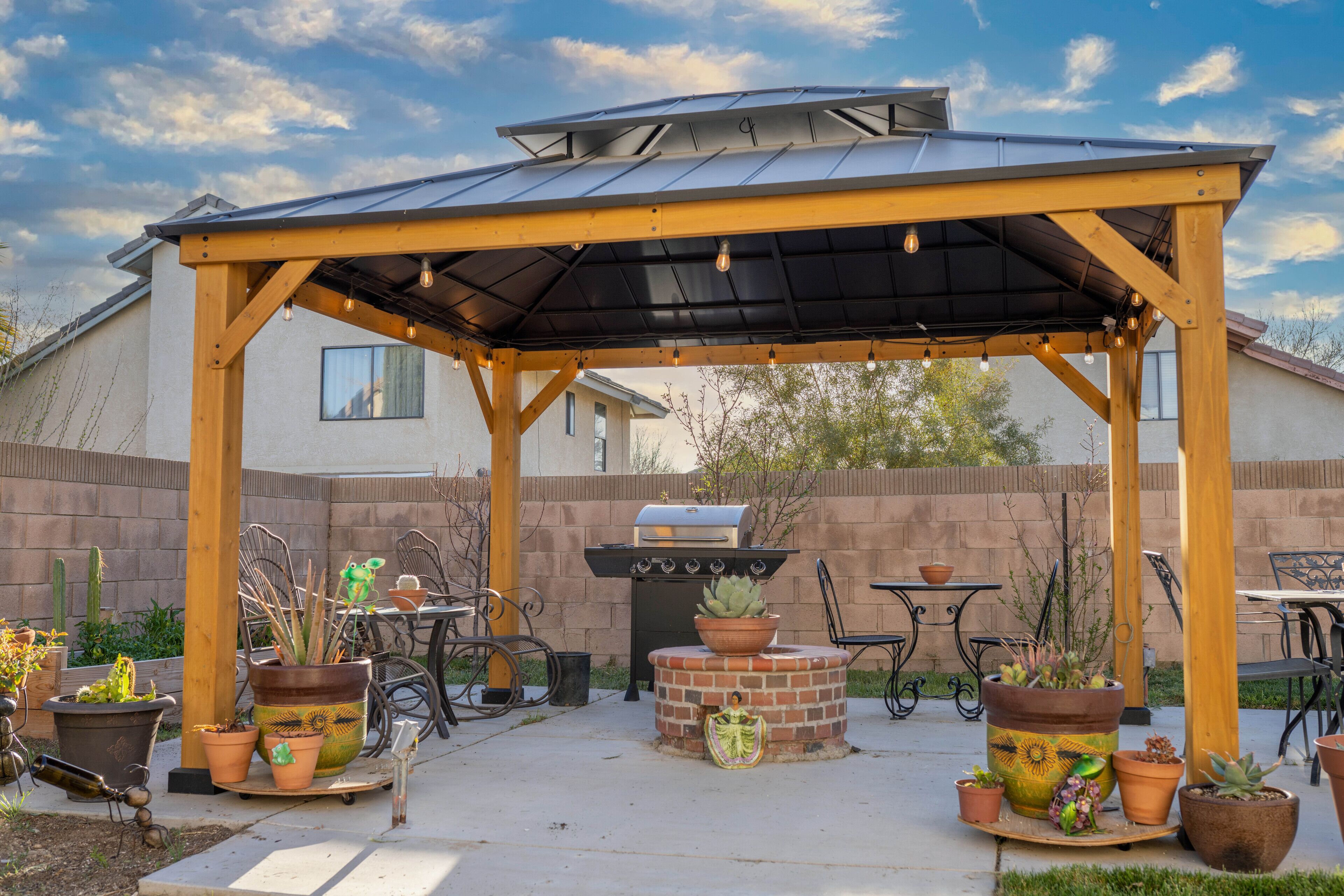 Un patio cubierto con una parrilla, plantas en macetas y mobiliario de exterior.