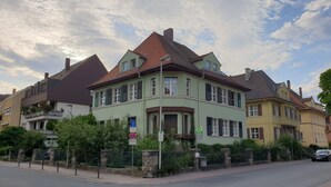 Ein zweistöckiges Haus mit grüner Fassade, zahlreichen Fenstern und einem roten Dach.