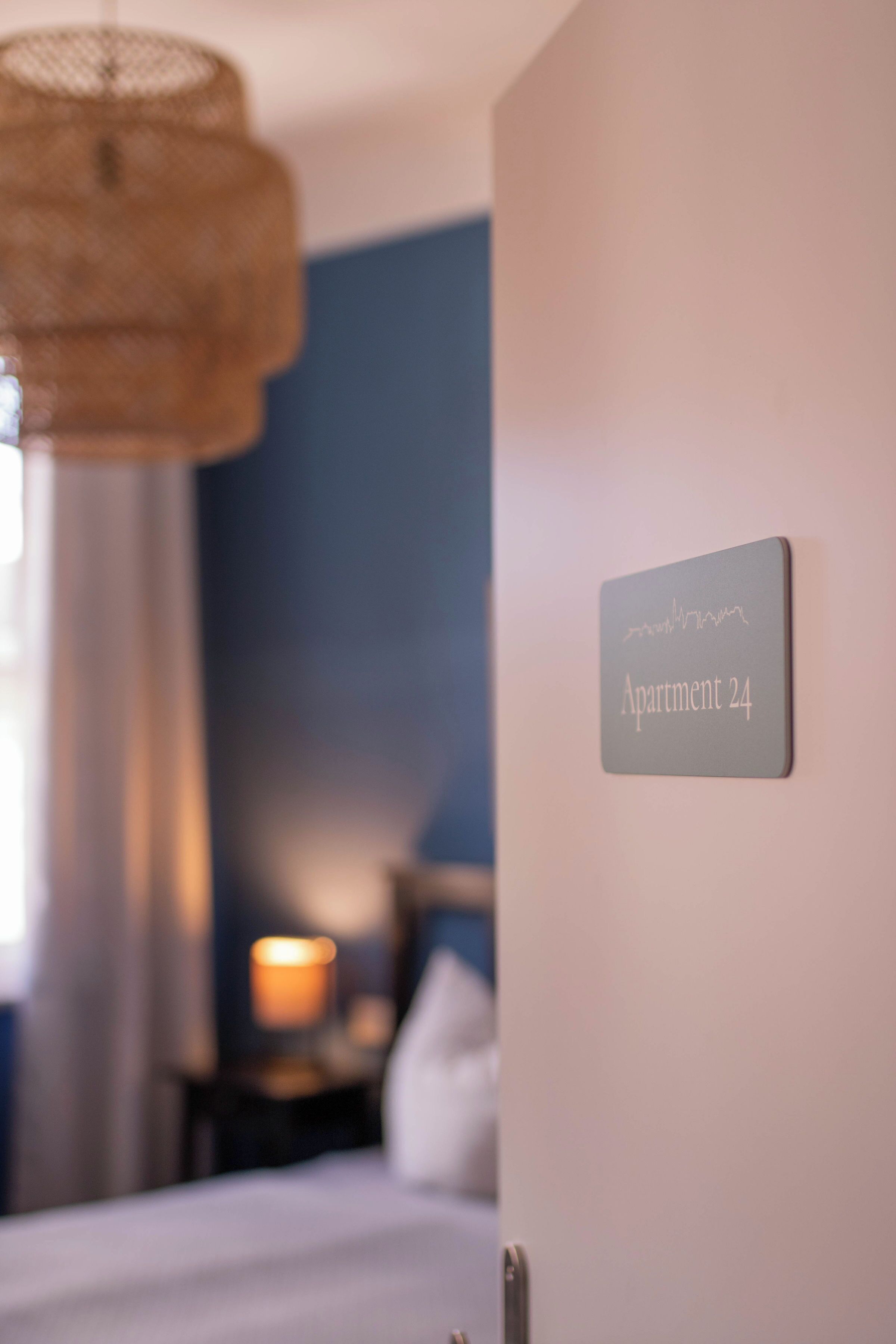 A sign indicating 'Apartment 24' in a hotel room with a bed, a nightstand, and a lamp.