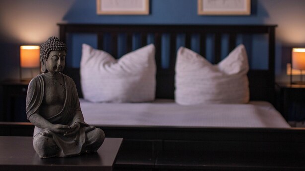 Ein Schlafzimmer mit einem Bett, einer Buddha-Statue und zwei gerahmten Bildern an der Wand.