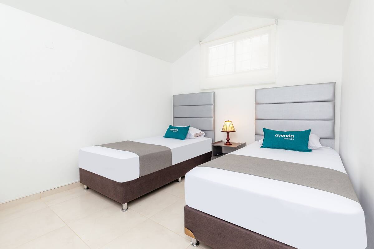Una habitación de hotel con dos camas, cada una con cabecero gris y almohada verde azulada.