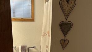 A bathroom with a shower curtain, a towel rack with towels, and decorative heart-shaped wall art. - Elk Run-Entire basement-1000 sq ft.-Cleaning fee included.  Sleeps 4-6. (Driggs)