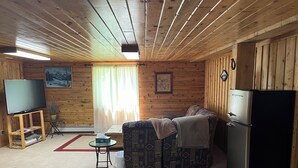 A cozy cabin interior with a sofa, a television on a wooden stand, a refrigerator, and a window with curtains. - Elk Run-Entire basement-1000 sq ft.-Cleaning fee included.  Sleeps 4-6. (Driggs)
