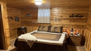 A cozy wooden cabin bedroom with a bed, a nightstand, a lamp, and a sign on the wall. - Elk Run-Entire basement-1000 sq ft.-Cleaning fee included.  Sleeps 4-6. (Driggs)