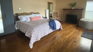 Ein Schlafzimmer mit Bett, Holzboden, Deckenventilator, Kamin und einer Tür.