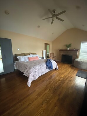 A bedroom with a bed, wooden flooring, a ceiling fan, a fireplace, and a door. - Beautiful Waterfront Getaway  (Olympia)