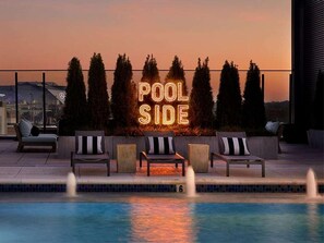 Ett område vid poolen med en neonreklamskylt som visar texten ”POOL SIDE”, solstolar och en pool med vattenstrålar.