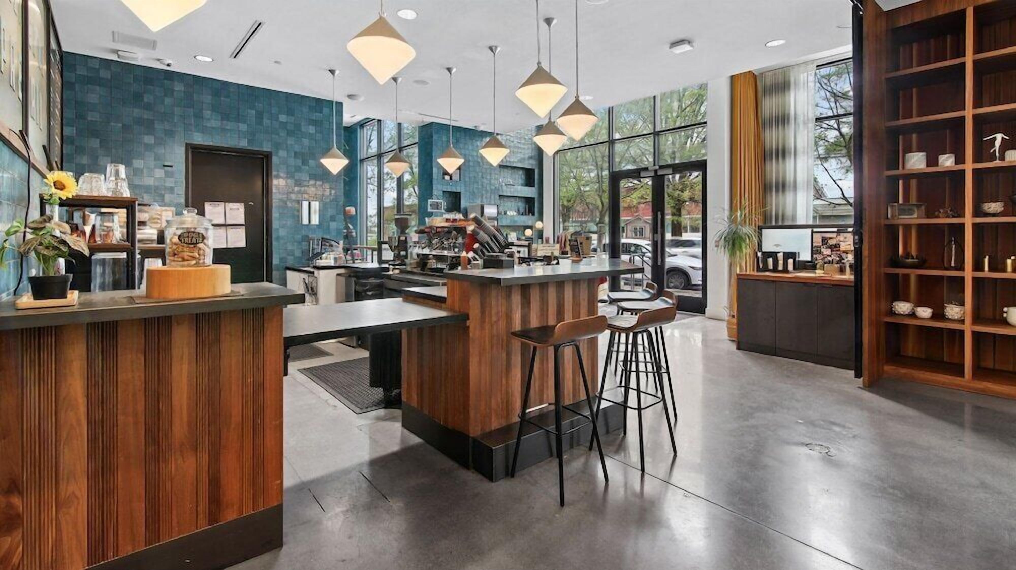A modern bar area with a wooden counter, bar stools, pendant lighting, and a view of the street outside.