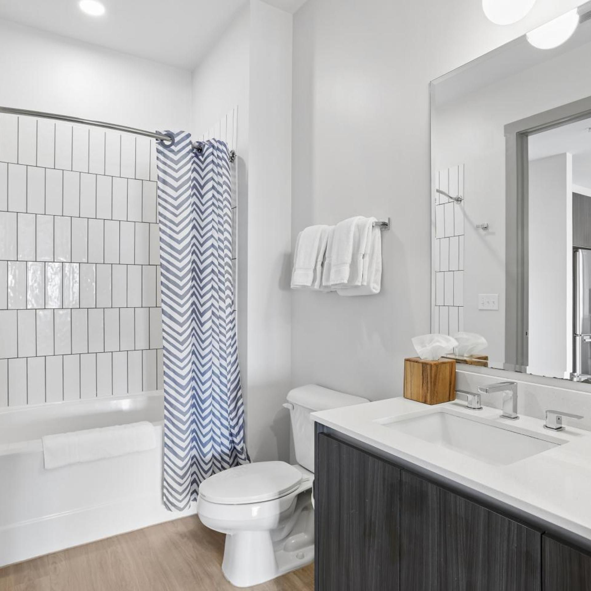 Un baño moderno con ducha de azulejos blancos, inodoro blanco y tocador con espejo.