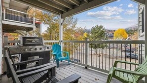 En overdækket terrasse med grill, to Adirondack-stole og udsigt til gaden og træerne.