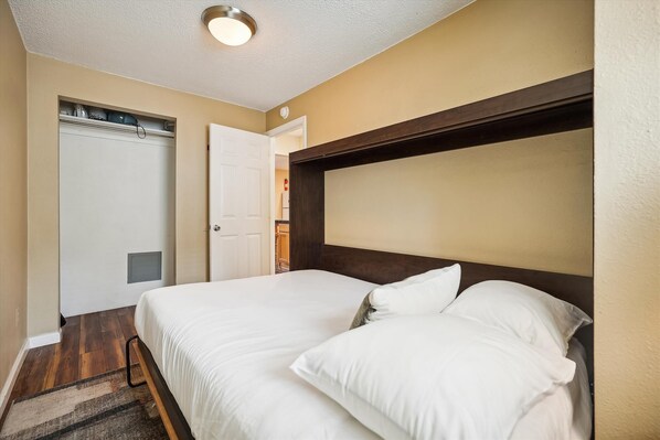 Een hotelkamer met een tweepersoonsbed, een houten hoofdbord, een witte deur en een plafondlamp.