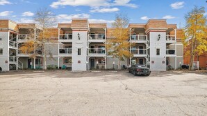 En bygning med flere etager, altaner, parkeringsplads og efterårsblade.