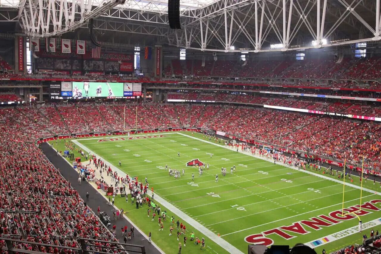 A large indoor stadium with multiple levels of seating, a football field, and a crowd of spectators.