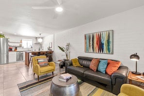 Uma sala de estar moderna com sofá, poltrona, mesa de centro e um espaço de refeições com mesa e cadeiras.