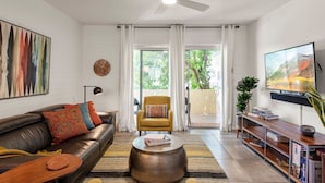 A living room with a sofa, armchair, coffee table, TV, and a balcony with curtains. - HeatedPool, Upscale in OldTown Scottsdale (Scottsdale)