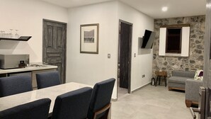 Une cuisine moderne dotée d’un four encastré, un coin repas avec une table et des chaises, un mur en pierre et un téléviseur fixé au mur.