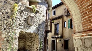 Une ruelle étroite pavée de pierres, bordée de bâtiments en pierre, avec une arche en briques et une fontaine.