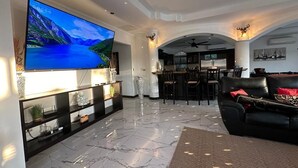 Ein geräumiges Wohnzimmer mit großem Flachbildfernseher, einem schwarzen Ledersofa und einem Marmorboden.
