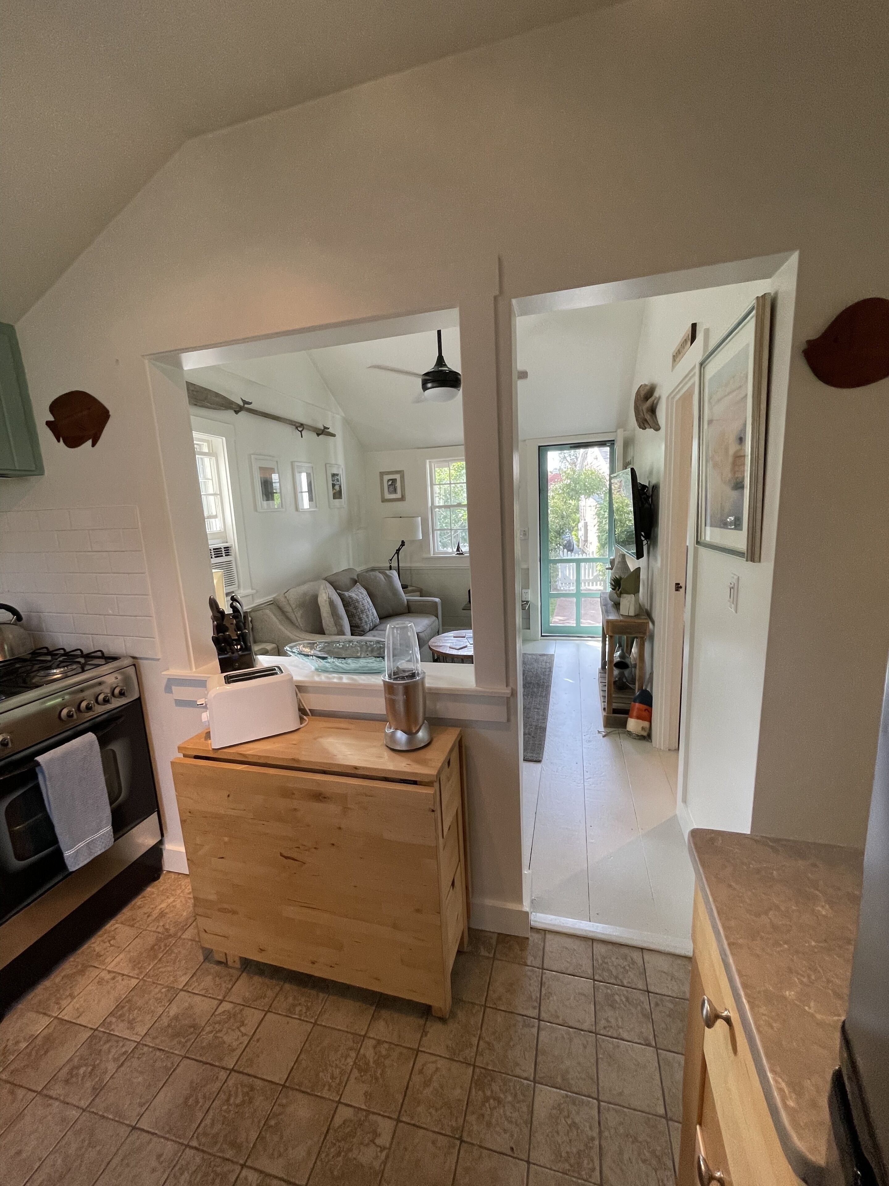 Una cocina con estufa, tostadora y encimera de madera. Se ve un espejo que refleja una sala de estar con sofá y ventilador de techo.