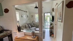 Una cocina con estufa, tostadora y encimera de madera. Se ve un espejo que refleja una sala de estar con sofá y ventilador de techo.