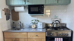 Cocina compacta con gabinetes verde azulado, un microondas, un tostador, un hervidor y una estufa a gas.